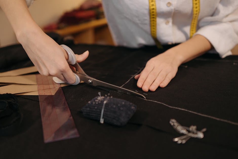 A tailor cutting black fabric with scissors in a workspace, focus on hands.