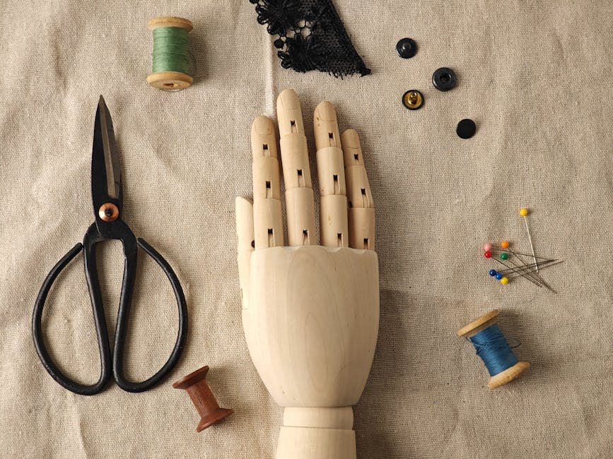 A flat lay of vintage sewing tools and a wooden hand mannequin on linen fabric.
